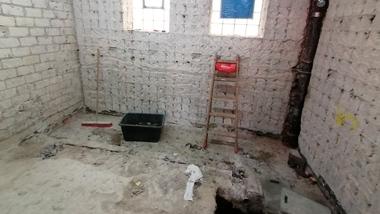 Rohbau eines Raumes mit freiliegenden Wänden, einer Leiter, einem Eimer und einem Bodenloch.