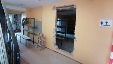 Innenansicht eines Raums mit durchbrochener Wand, Trennwänden und einem Schild zur Umkleide.