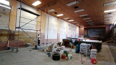 Baukräfte arbeiten in einem renovierungsbedürftigen Raum mit Gerüst, Werkzeugen und Baustellenmaterial.