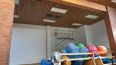 Heller Raum mit Holzdecke, einem Gerüst und bunten Bällen auf einer blauen Fläche. Weiße Wände im Hintergrund.