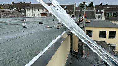 Nahaufnahme von weißen Baustellenmaterialien auf einem flachen Dach mit grauer Abdeckung und Häusern im Hintergrund.