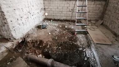 Baustelle mit freigelegtem Erdreich, Treppe, Rohren und Kabeln an einer Mauer aus Betonsteinen.