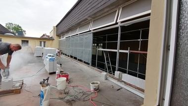Bauarbeiter schneidet Baustellenmaterial auf einer Terrasse, umgeben von Bauutensilien und einem Gerüst.