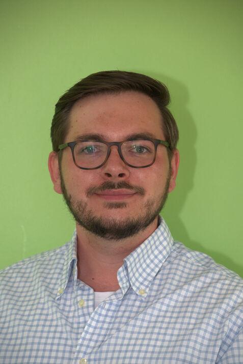 Porträt eines Mannes mit Brille und einem karierten Hemd vor grüner Wand.