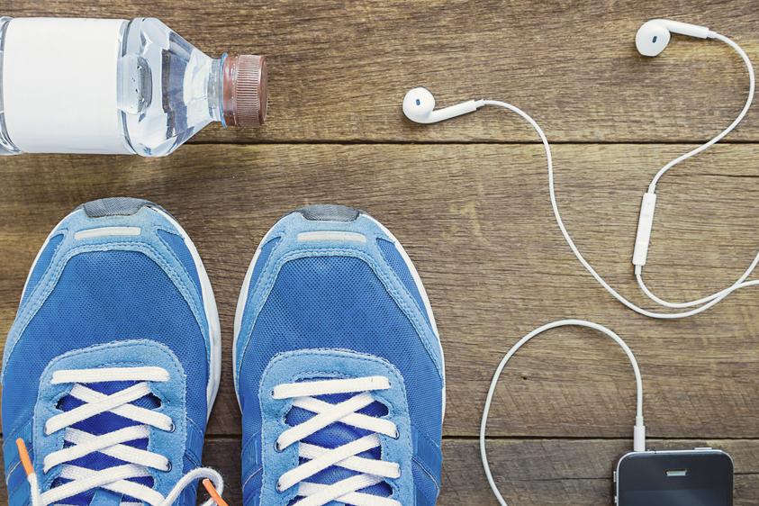 Blick von oben auf blaue Sportschuhe, Wasserflasche, Kopfh&ouml;rer und ein Smartphone auf einer Holzoberfl&auml;che.