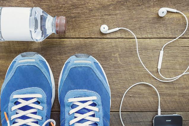 Blick von oben auf blaue Sportschuhe, Wasserflasche, Kopfh&ouml;rer und ein Smartphone auf einer Holzoberfl&auml;che.