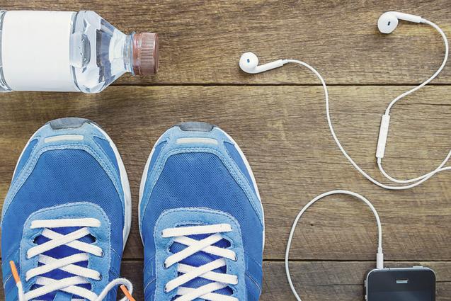 Blick von oben auf blaue Sportschuhe, Wasserflasche, Kopfh&ouml;rer und ein Smartphone auf einer Holzoberfl&auml;che.