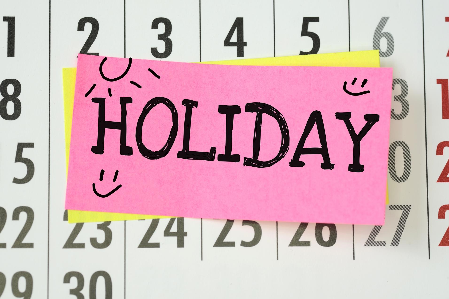 Bunte Haftnotiz mit dem Wort „HOLIDAY“ auf einem Kalenderblatt mit Datumsangaben.