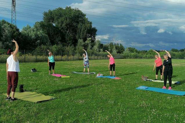 6 Frauen auf einer Wiese die ihre Matte vor sich liegen haben und Sport&uuml;bungen machen.