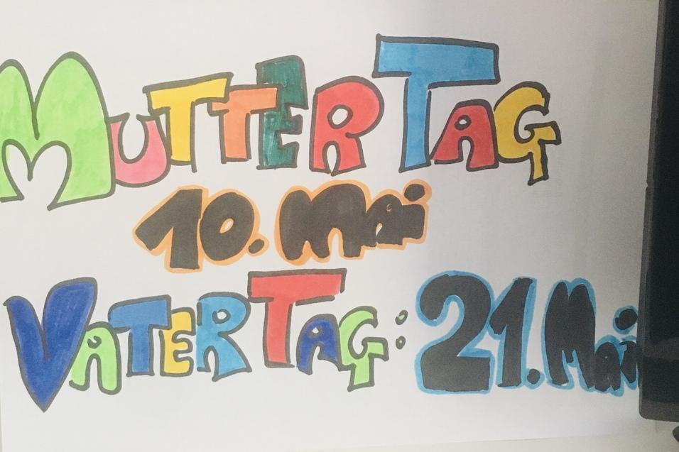 Bunt beschriftetes Papier mit &bdquo;Muttertag 10. Mai&ldquo; und &bdquo;Vattertag 21. Mai&ldquo; steht neben einer Blumenvase mit Tulpen.
