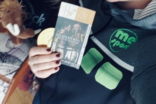 Zwei Frauen posieren nah beieinander und halten eine Eintrittskarte und ein Stofftier vor einem B&uuml;cherregal.