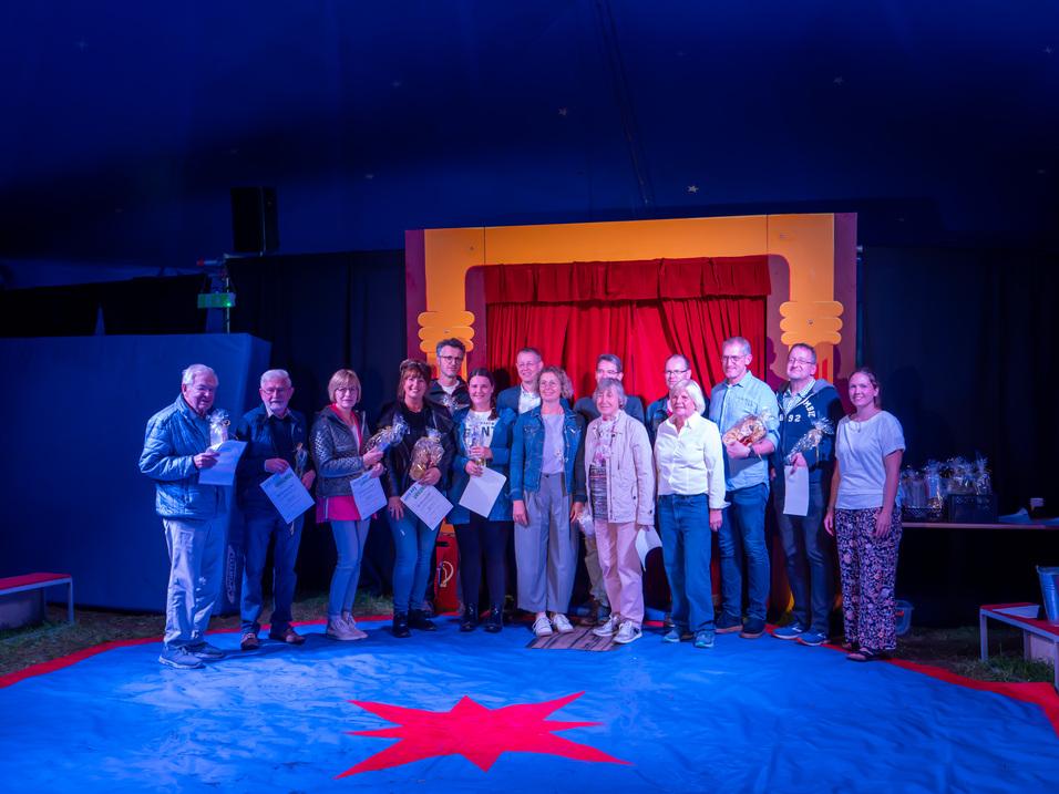 Gruppenfoto im Zirkuszelt.Insgesamt sind fünfzehn Personen drauf abgebildet.