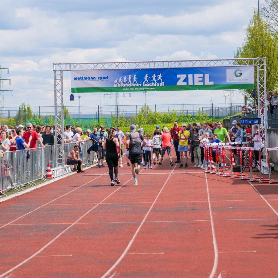 Läufer erreichen das Ziel bei einer Sportveranstaltung, umgeben von jubelnden Zuschauern auf der Tribüne.