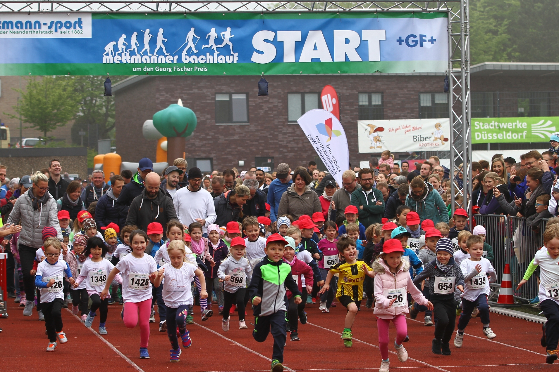 Startschuss f&uuml;r den Mettmanner Bachlauf: Kinder in bunten Laufshirts und roten Caps sprinten auf einer Laufbahn los.