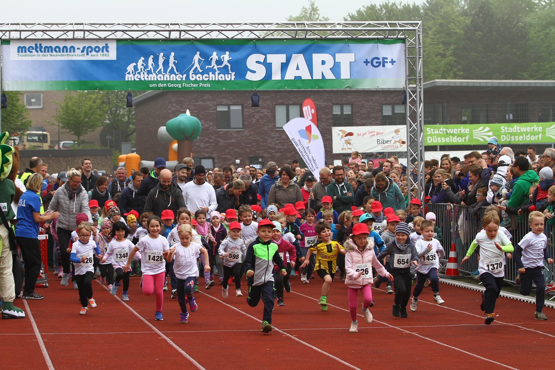 Startschuss für den Mettmanner Bachlauf: Kinder in bunten Laufshirts und roten Caps sprinten auf einer Laufbahn los.