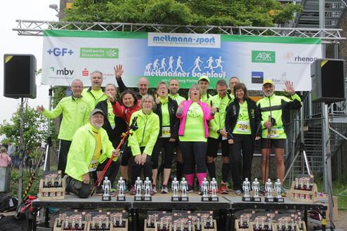 Gruppe von Sportlern in leuchtend grünen Shirts posiert auf einer Bühne vor einer Event-Serienwagen und Pokalen.