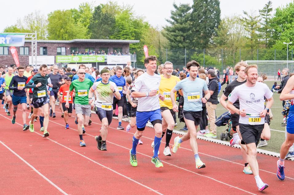 Start eines Laufwettbewerbs mit zahlreichen Teilnehmern auf einer roten Laufbahn unter einem Startbanner.