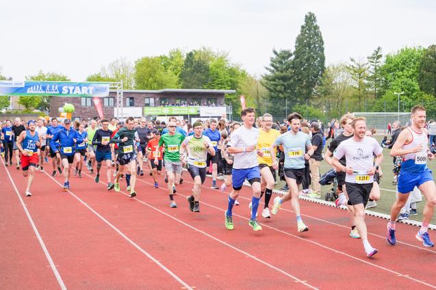 Start eines Laufwettbewerbs mit zahlreichen Teilnehmern auf einer roten Laufbahn unter einem Startbanner.