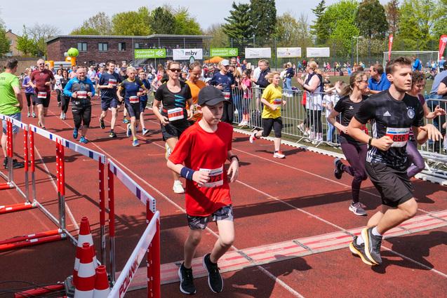 Sportveranstaltung mit Läufern beim Start eines Wettlaufs, umgeben von Zuschauern und einer begrünten Kulisse.