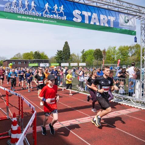 Sportveranstaltung mit Läufern beim Start eines Wettlaufs, umgeben von Zuschauern und einer begrünten Kulisse.