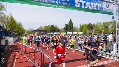 Sportveranstaltung mit Läufern beim Start eines Wettlaufs, umgeben von Zuschauern und einer begrünten Kulisse.