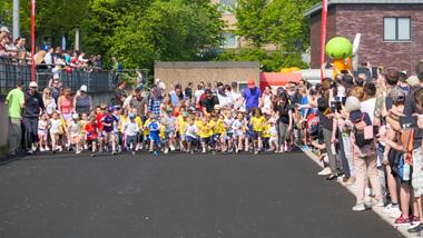 Eine Gruppe von Kindern startet einen Wettlauf, umringt von Zuschauern auf einer asphaltierten Strecke.