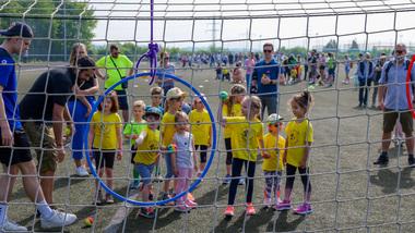 Gruppenspiel von Kindern in gelben T-Shirts auf einem Sportplatz mit einer blauen Zielscheibe im Vordergrund.