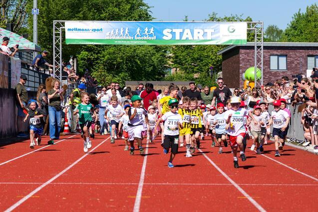 Start eines Kinderlaufes mit vielen laufenden Kindern auf einer roten Laufbahn, umgeben von jubelnden Zuschauern.