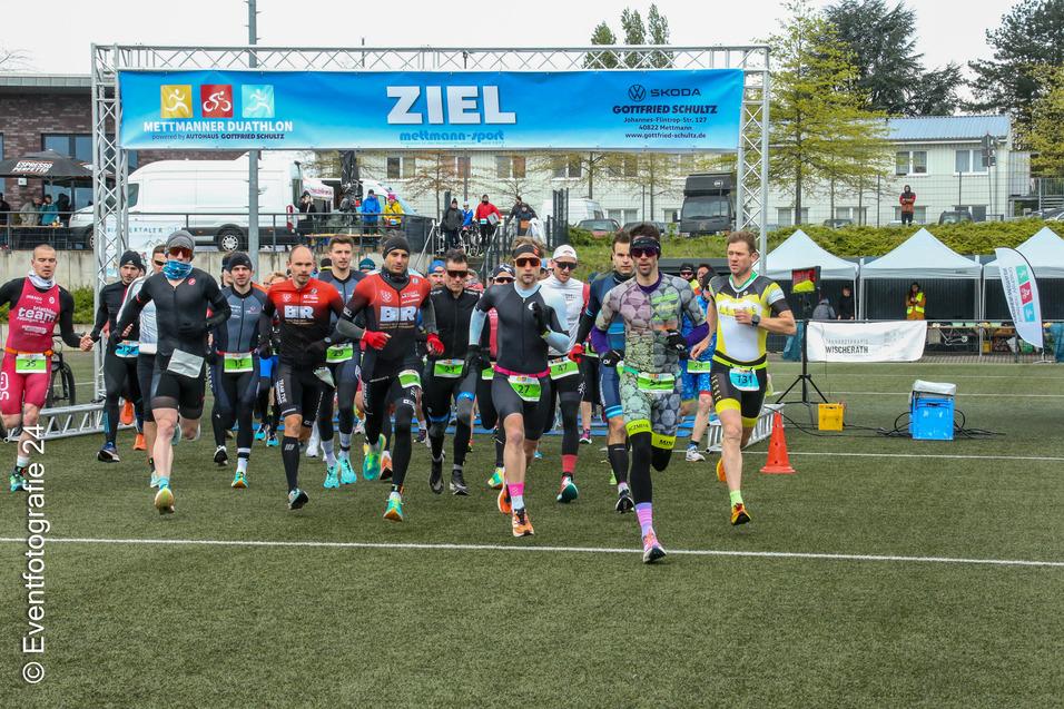 Start des Mettmanner Duathlons: Läufer in Sportkleidung laufen auf einem Rasenfeld unter einem Zielbanner.