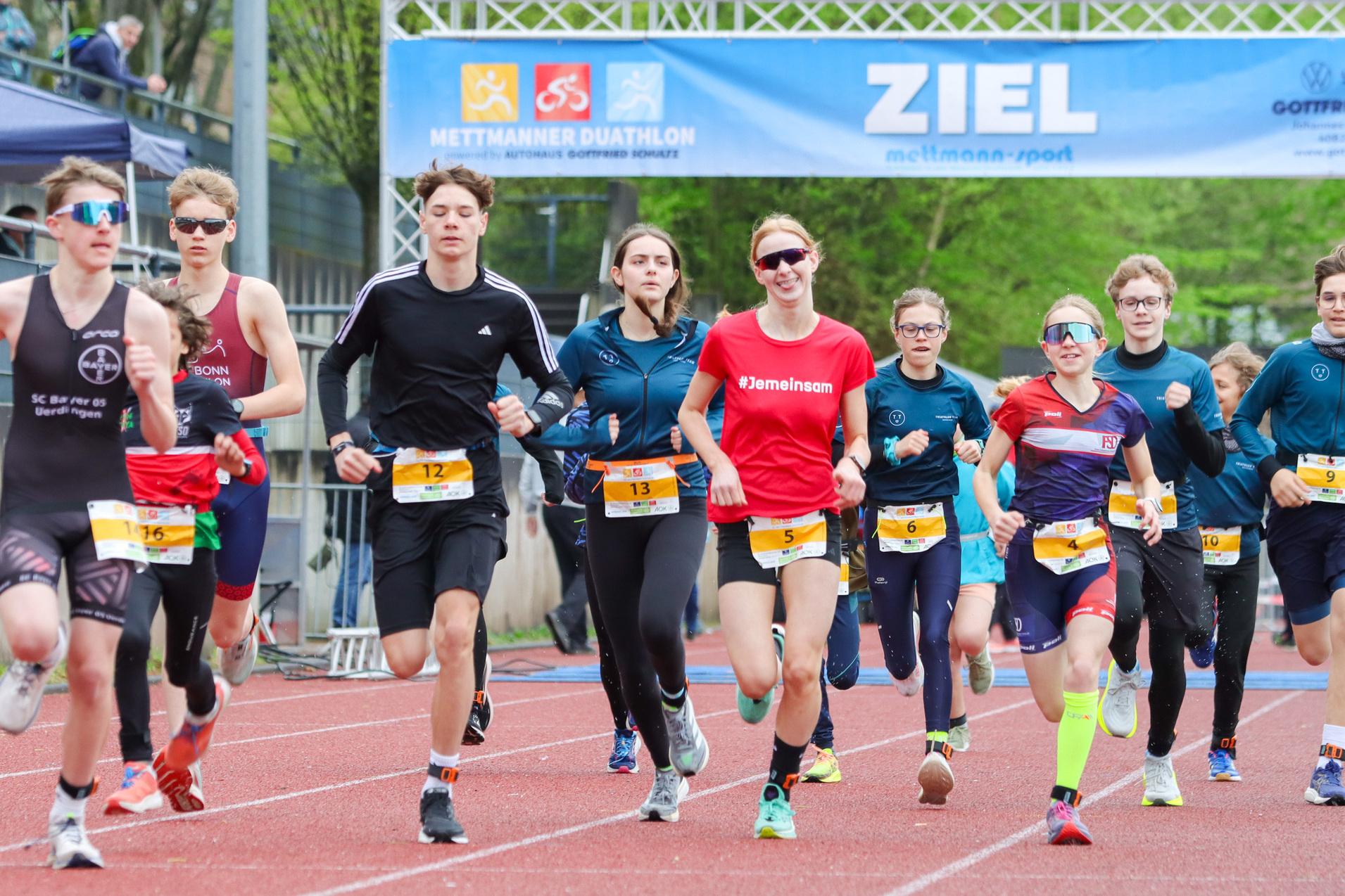 Eine Gruppe junger Läufer in Sportbekleidung rennt auf einer roten Tartanbahn zum Ziel beim Mettmanner Duathlon.
