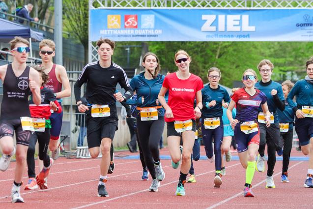Eine Gruppe junger Läufer in Sportbekleidung rennt auf einer roten Tartanbahn zum Ziel beim Mettmanner Duathlon.