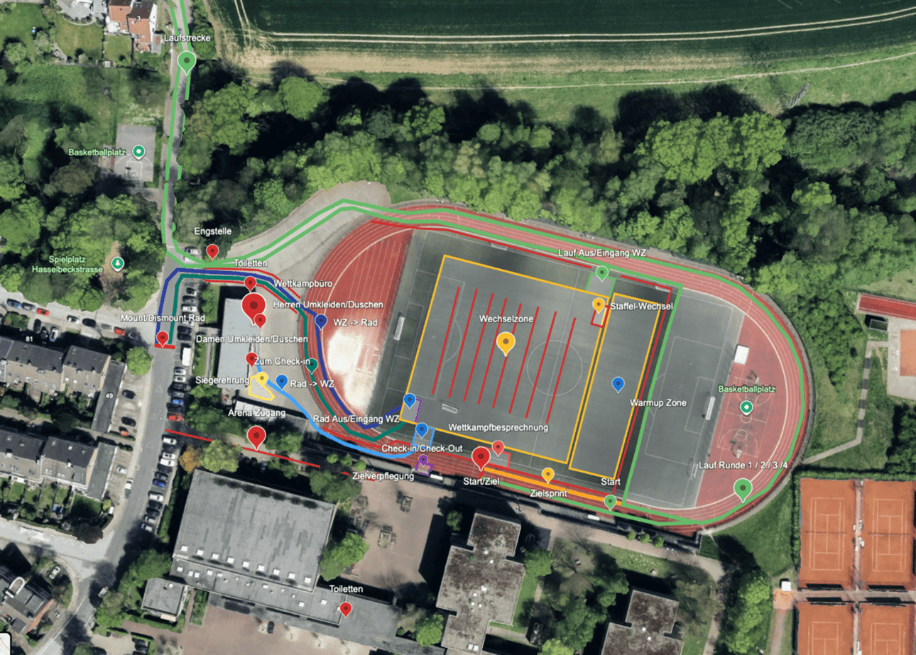 Luftaufnahme eines Sportgeländes mit Laufbahn, Fußballfeld, Umkleidebereichen und umliegenden Einrichtungen.