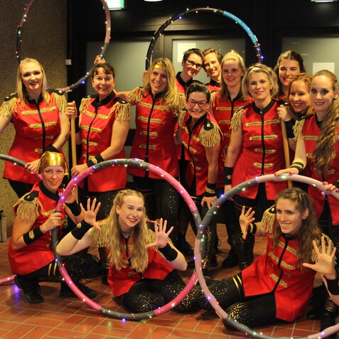 Gruppennahaufnahme von zw&ouml;lf Frauen in roten Kost&uuml;men mit Hula-Hoops, die fr&ouml;hlich in eine Kamera l&auml;cheln.