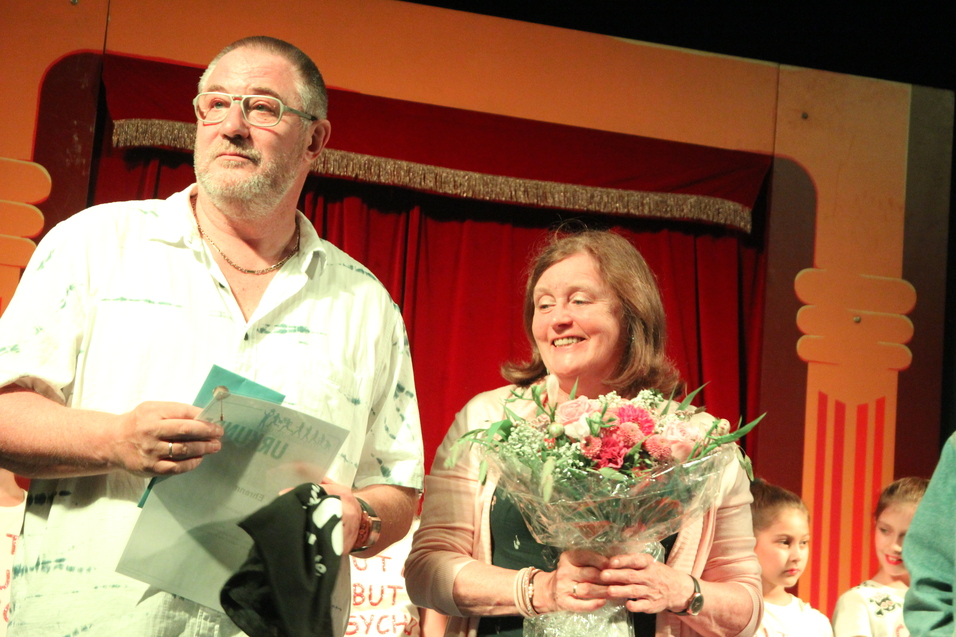 Ein Mann und eine Frau stehen auf einer Bühne, der Mann hält eine Urkunde, die Frau einen Blumenstrauß.