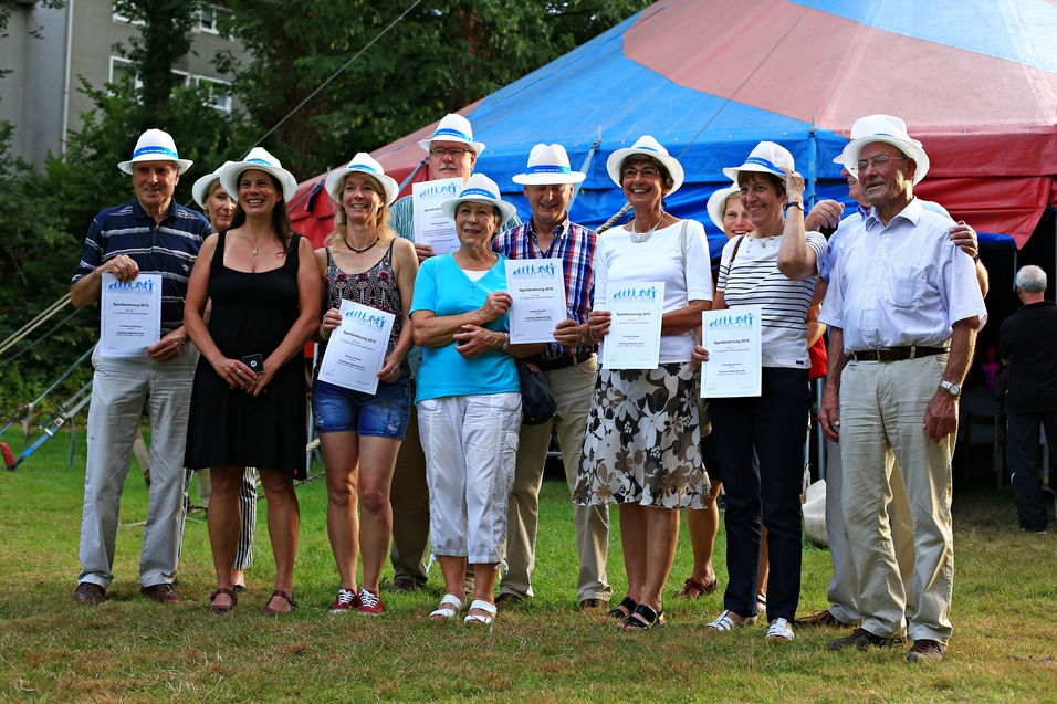 Gruppe von neun Personen mit Urkunden, alle tragen weiße Hüte, vor einem Zelt im Freien.