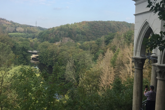 Blick auf bewaldete H&uuml;gel und eine flie&szlig;ende Wasserstra&szlig;e, im Vordergrund ein historisches Geb&auml;ude mit S&auml;ulen.