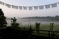 Blick von einem Balkon auf eine nebelige Landschaft mit Wiesen und Bäumen, dekoriert mit Wimpeln im Vordergrund.