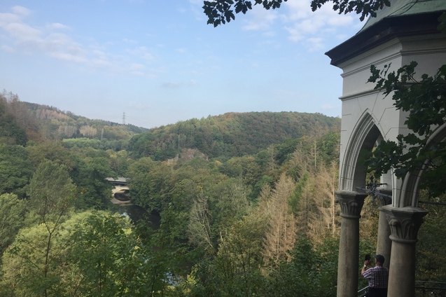Blick auf bewaldete Hügel und eine fließende Wasserstraße, im Vordergrund ein historisches Gebäude mit Säulen.