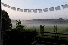 Blick von einem Balkon auf eine nebelige Landschaft mit Wiesen und Bäumen, dekoriert mit Wimpeln im Vordergrund.