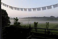 Blick von einem Balkon auf eine nebelige Landschaft mit Wiesen und Bäumen, dekoriert mit Wimpeln im Vordergrund.
