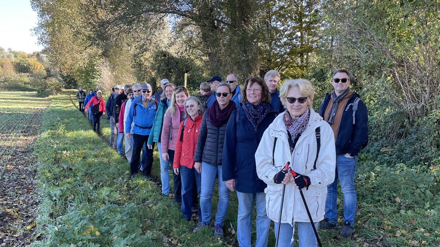 Gruppe von 20 Personen steht auf einem Pfad am Waldrand, umgeben von Bäumen und herbstlichem Laub.