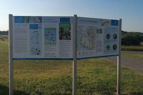 Informationstafel mit Karten und Texten &uuml;ber die Umgebung, auf einem Weg in der Natur aufgestellt.