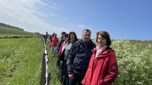 Gruppe von Menschen steht an einem Zaun auf einer Wiese unter einem blauen Himmel mit wenigen Wolken.