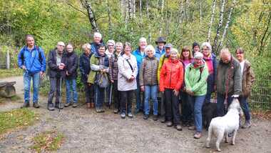 Gruppenselfie eines Wanderteams mit 20 Personen und zwei Hunden in einer herbstlichen Waldlandschaft.