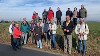 Gruppe von 20 Wanderern mit Stöcken, auf einer Wiese stehend, bei sonnigem Wetter mit blauem Himmel.