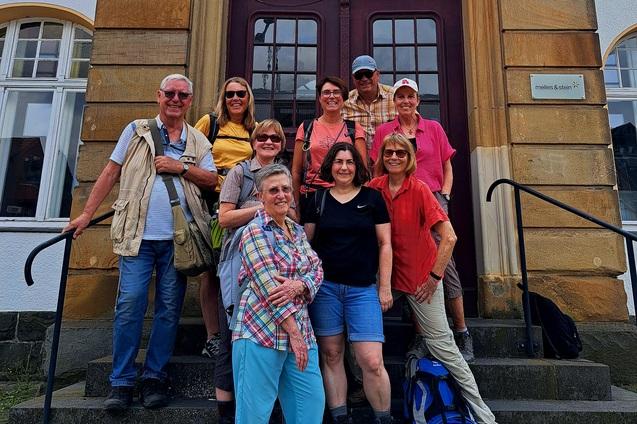 Gruppe von neun Personen auf Stufen vor einem historischen Gebäude, alle in Freizeitkleidung und lächelnd.