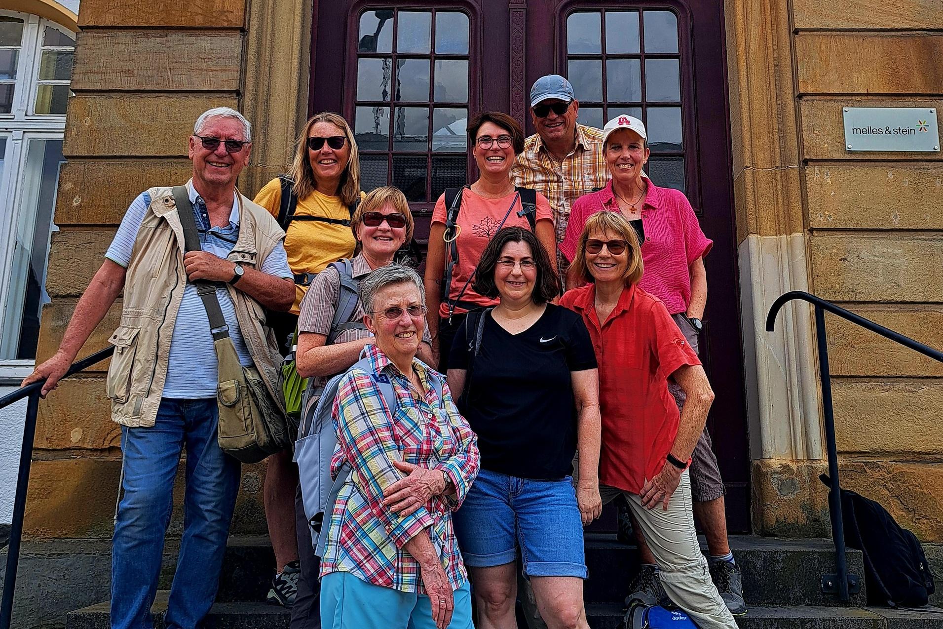 Gruppe von neun Personen auf Stufen vor einem historischen Gebäude, alle in Freizeitkleidung und lächelnd.
