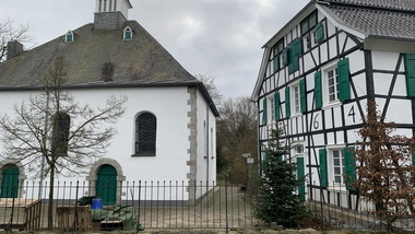 Zwei historische Gebäude, eines mit einem spitzen Dach und das andere mit Fachwerk und grünen Fensterläden.