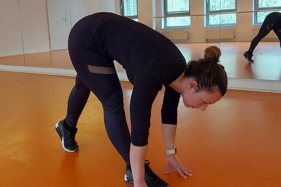 Frau beugt sich vor und streckt die Hände auf einem orangen Boden in einem Spiegelraum.