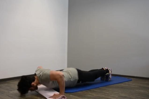 Mann macht Liegestütze auf einer blauen Gymnastikmatte in einem hellen Raum mit Holzboden.